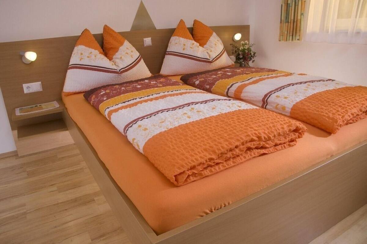 A double bed with a wooden headboard, orange bedding, and decorative pillows.