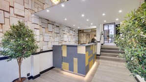 A reception area with a modern design, featuring a geometric patterned wall, a reception desk, and potted plants. - Hotel Lucien & Marinette (Paris)