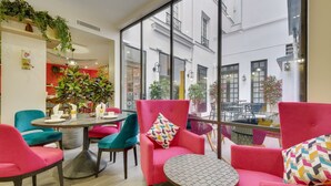 A modern interior with vibrant seating, a round table, and large windows offering views of the street. - Hotel Lucien & Marinette (Paris)