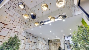 A modern interior with geometric wall patterns, multiple pendant lights, and indoor plants. - Hotel Lucien & Marinette (Paris)