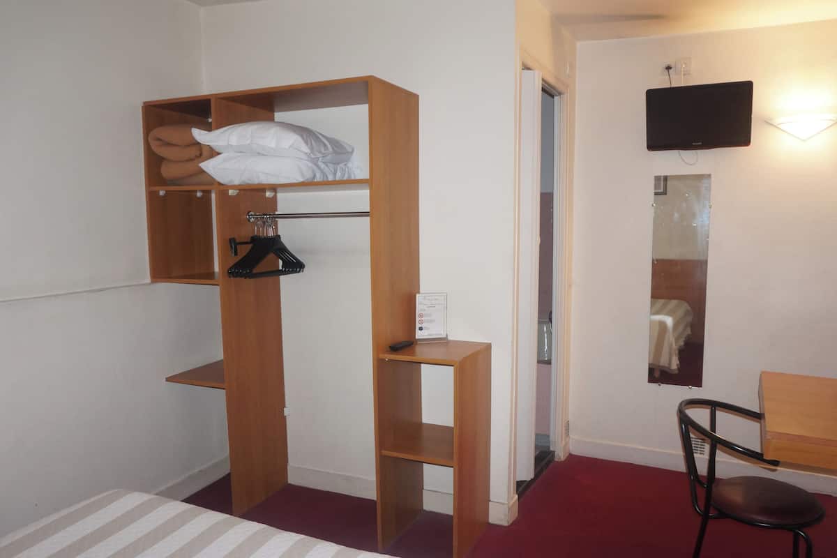 Ein Zimmer mit einem Bett, einem Holzschrank, einem Schreibtisch, einem Sessel, einem Spiegel und einem Fernseher.