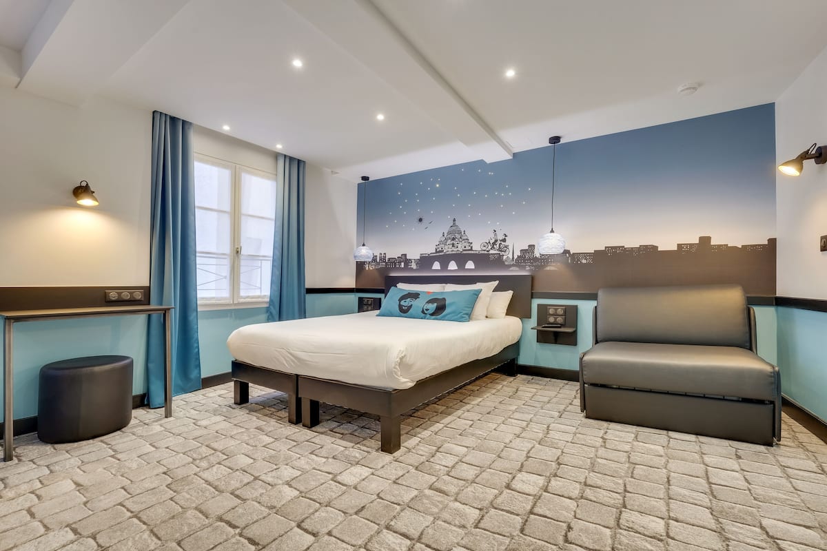 Ein Hotelzimmer mit Bett, Schreibtisch, Stuhl und einem Stadtbild-Wandgemälde.