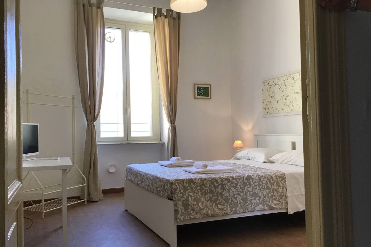 A bedroom with a bed, bedside lamp, and a desk with a computer.