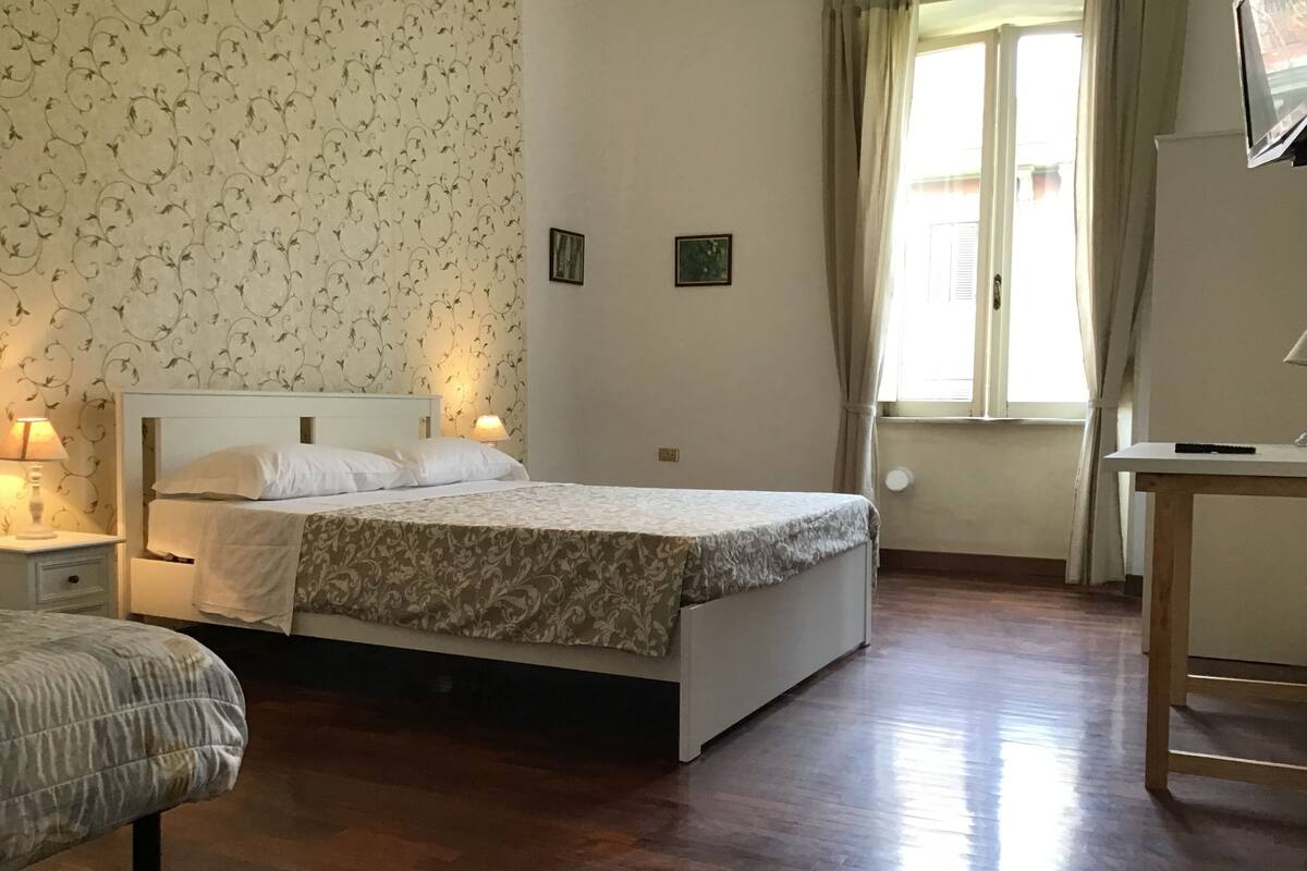 A bedroom with a bed, bedside tables, a desk, and a window with curtains.