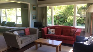 A living room with a grey sofa, a red sofa, a wooden coffee table, and a black armchair. There is a window with a view of greenery outside.