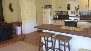 A compact kitchen with a central island, wooden stools, a stove, a toaster, and a refrigerator.