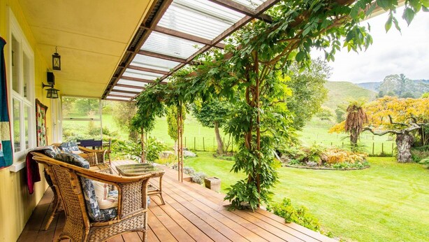A covered outdoor area with wicker furniture and a view of a well-maintained garden.