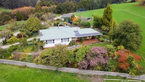 A house with a green roof, surrounded by lush gardens and trees, set in a hilly landscape.