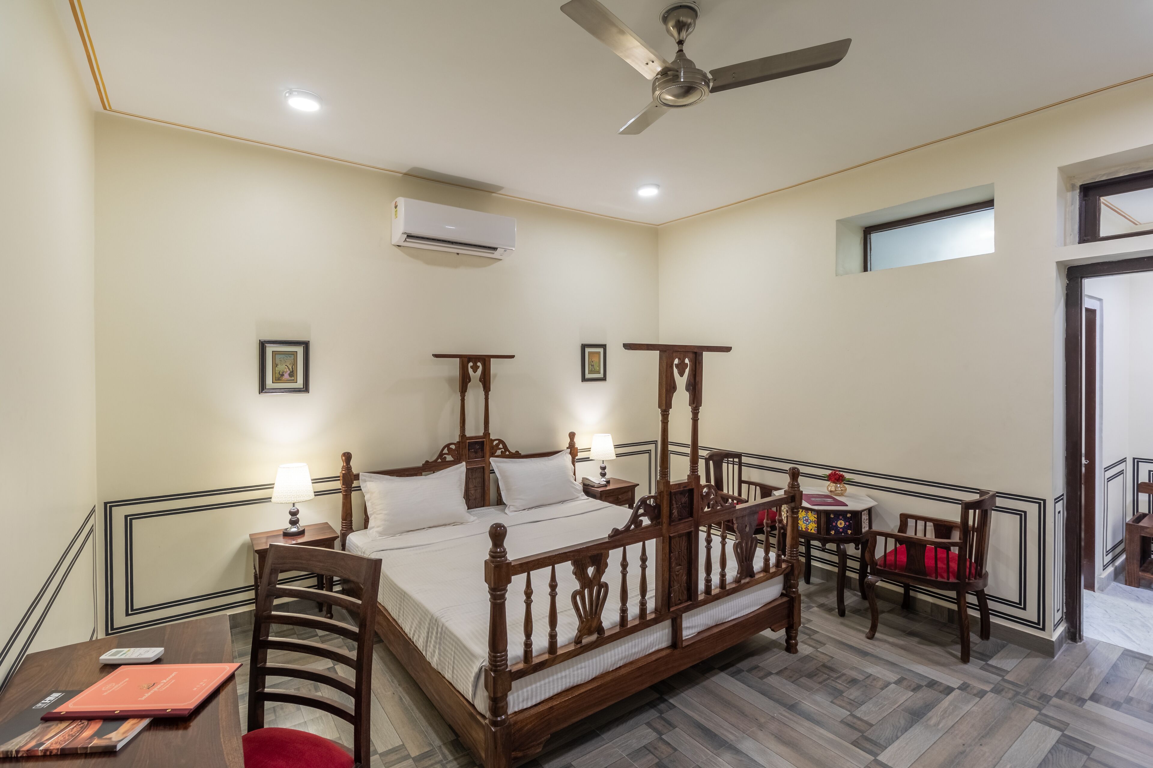 A bedroom with a four-poster bed, a desk with a chair, a small table with a lamp, and a ceiling fan.