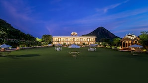 A large, illuminated building with a symmetrical facade, surrounded by a well-maintained lawn and outdoor seating areas.