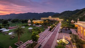 A hotel with a large garden, a fountain, and a view of the mountains.