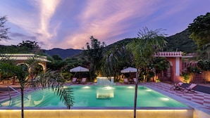 A swimming pool with a checkered border, surrounded by lounge chairs and umbrellas, set against a mountainous backdrop.