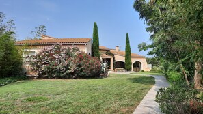 A house with a tiled roof, a garden with various plants, and a pathway leading to the entrance.