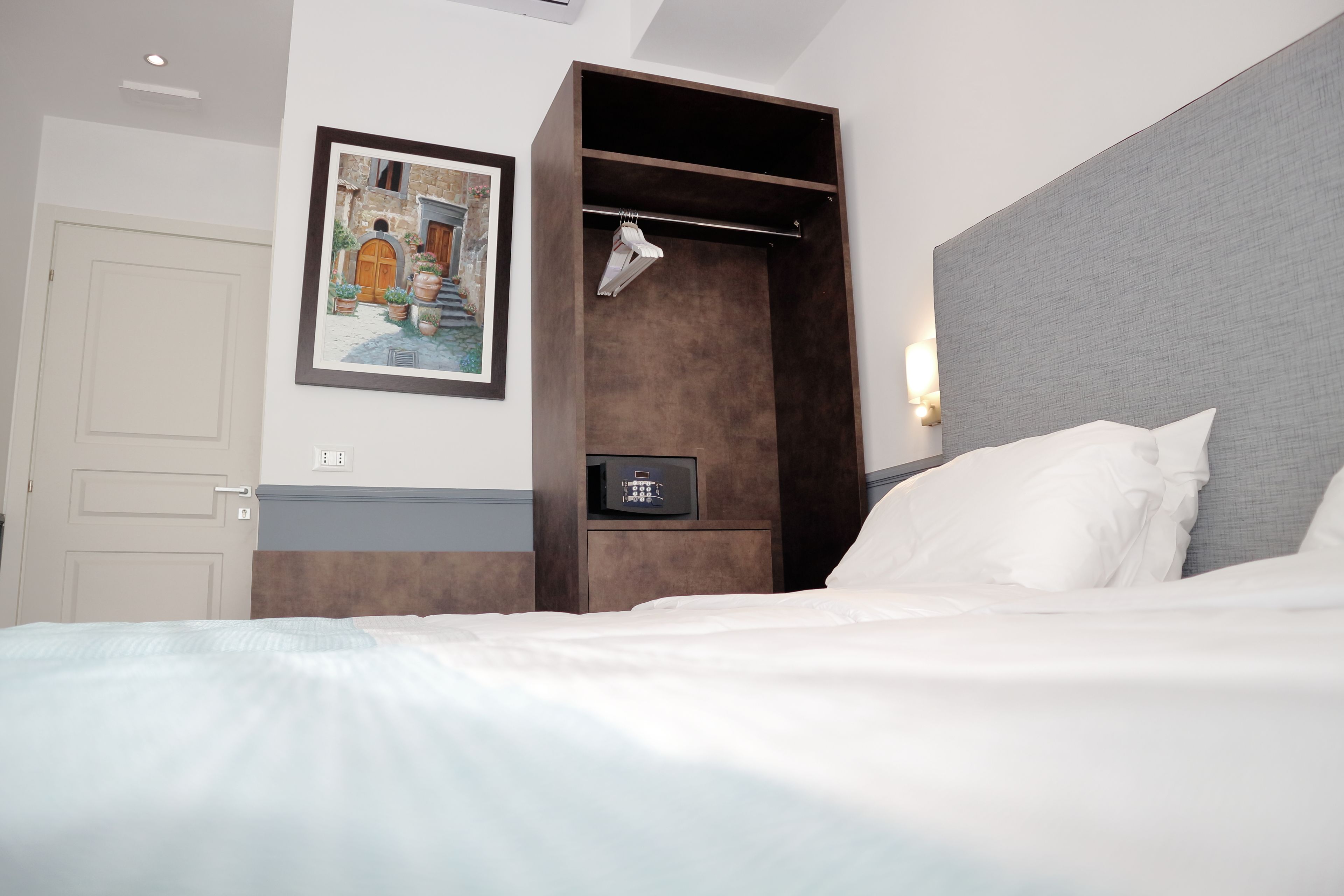 Quarto de hotel com cama, cabideiro, pintura e painel de controle.
