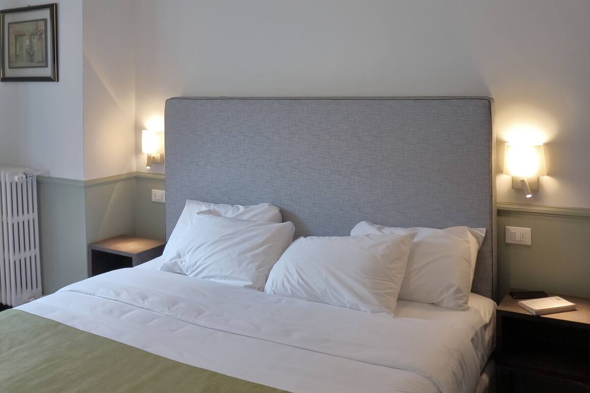 A neatly made bed with white linens and a green throw, a grey headboard, and two bedside lamps.