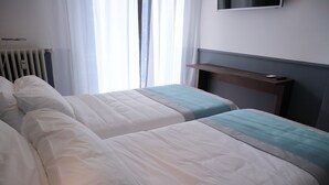 A hotel room with two beds, a radiator, a TV mounted on the wall, and a window with curtains. - Dimora dell'Arte B&B (Sesto San Giovanni)