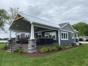 A two-story house with a covered porch, stone pillars, and a view of a lake.