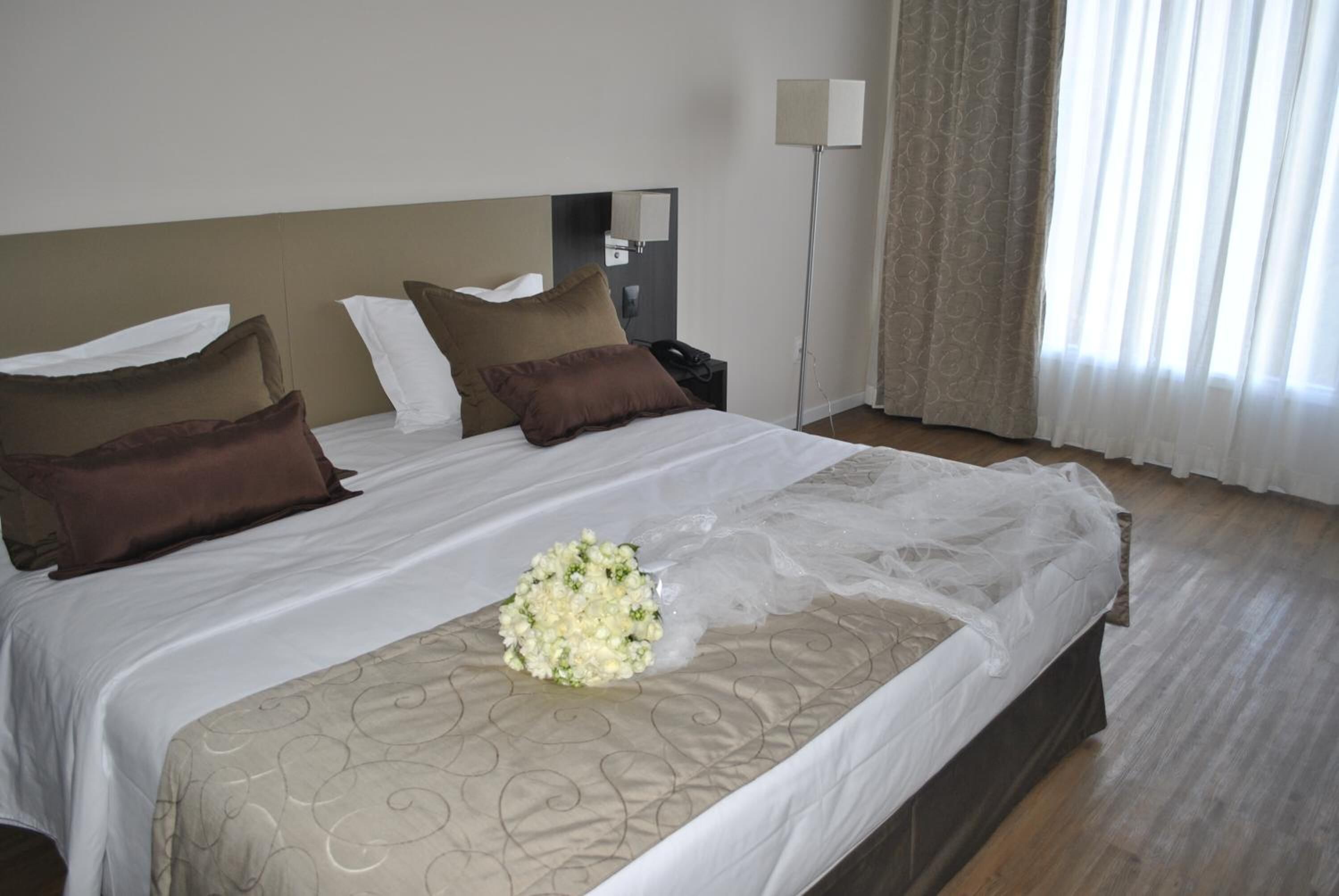 A hotel room with a large bed, a bedside table, a lamp, and a window with curtains.