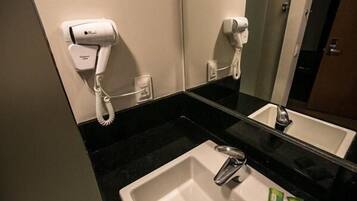 A hotel bathroom with a white sink, a hairdryer, and a phone mounted on the wall.