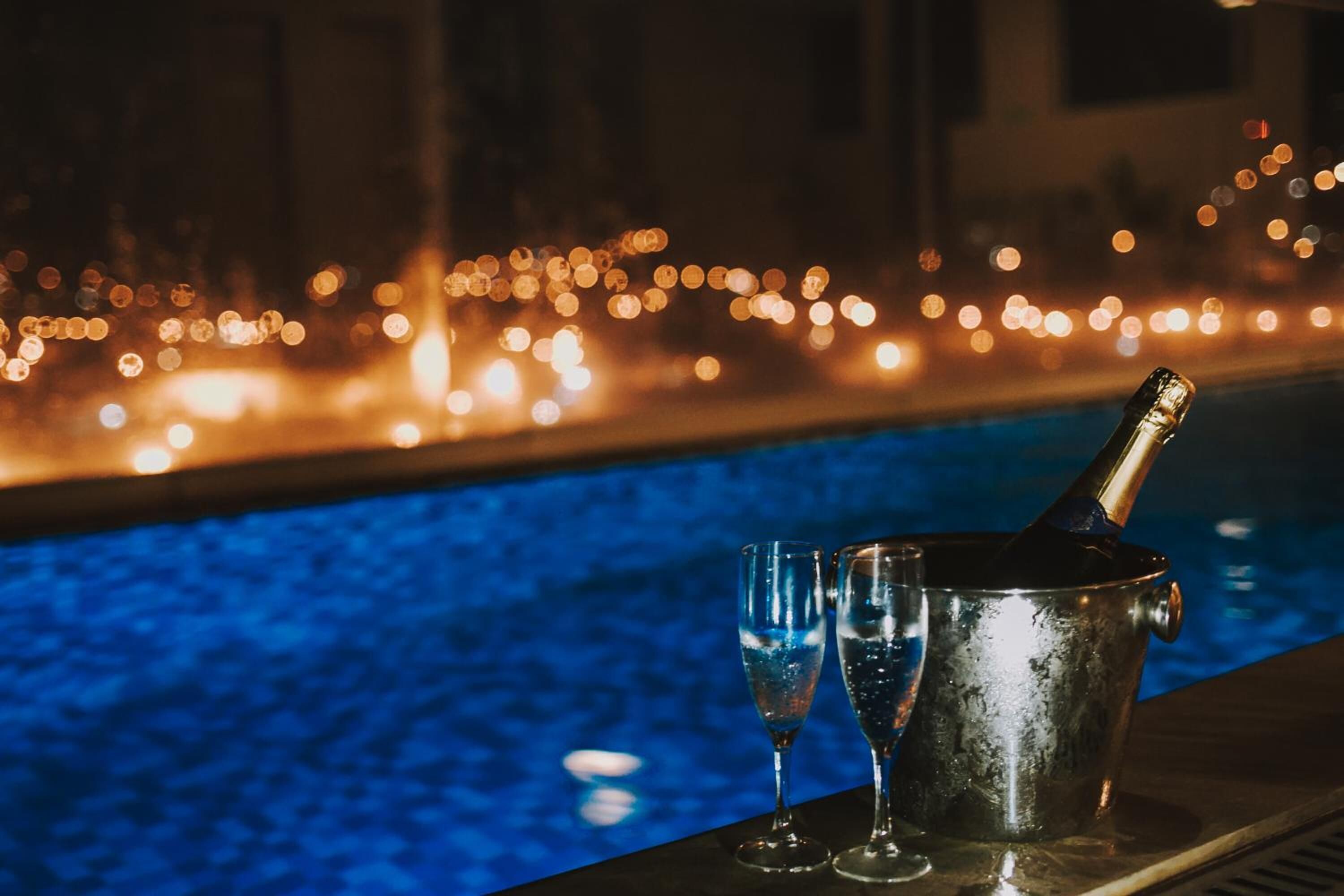 Une scène se déroulant au bord d’une piscine, avec une bouteille de champagne et des verres, évoquant une ambiance festive ou détendue.