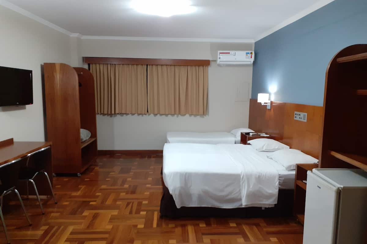 Ein Hotelzimmer mit zwei Betten, einem Schreibtisch, einem Stuhl, einem Fernseher, einer Klimaanlage und einem Kühlschrank.