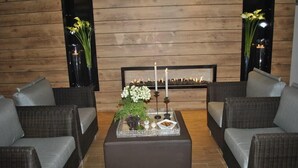 Eine gemütliche Sitzecke mit Korbuscheln und einem Tisch, auf dem eine Blumenkomposition und Kerzen stehen.