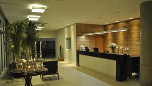 Ein moderner Empfangsbereich mit einem Holzbüro, einem runden Tisch mit Kerzen und einer großen Topfpflanze.