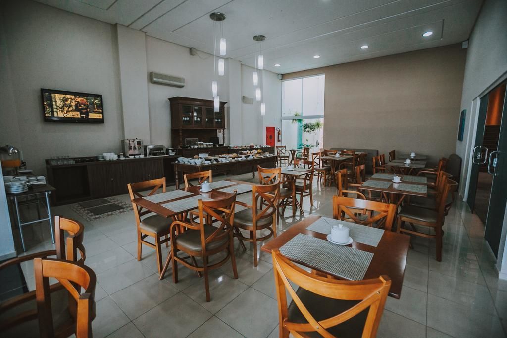 Un restaurante con mesas y sillas de madera, una zona de cocina y un amplio ventanal que proporciona luz natural.