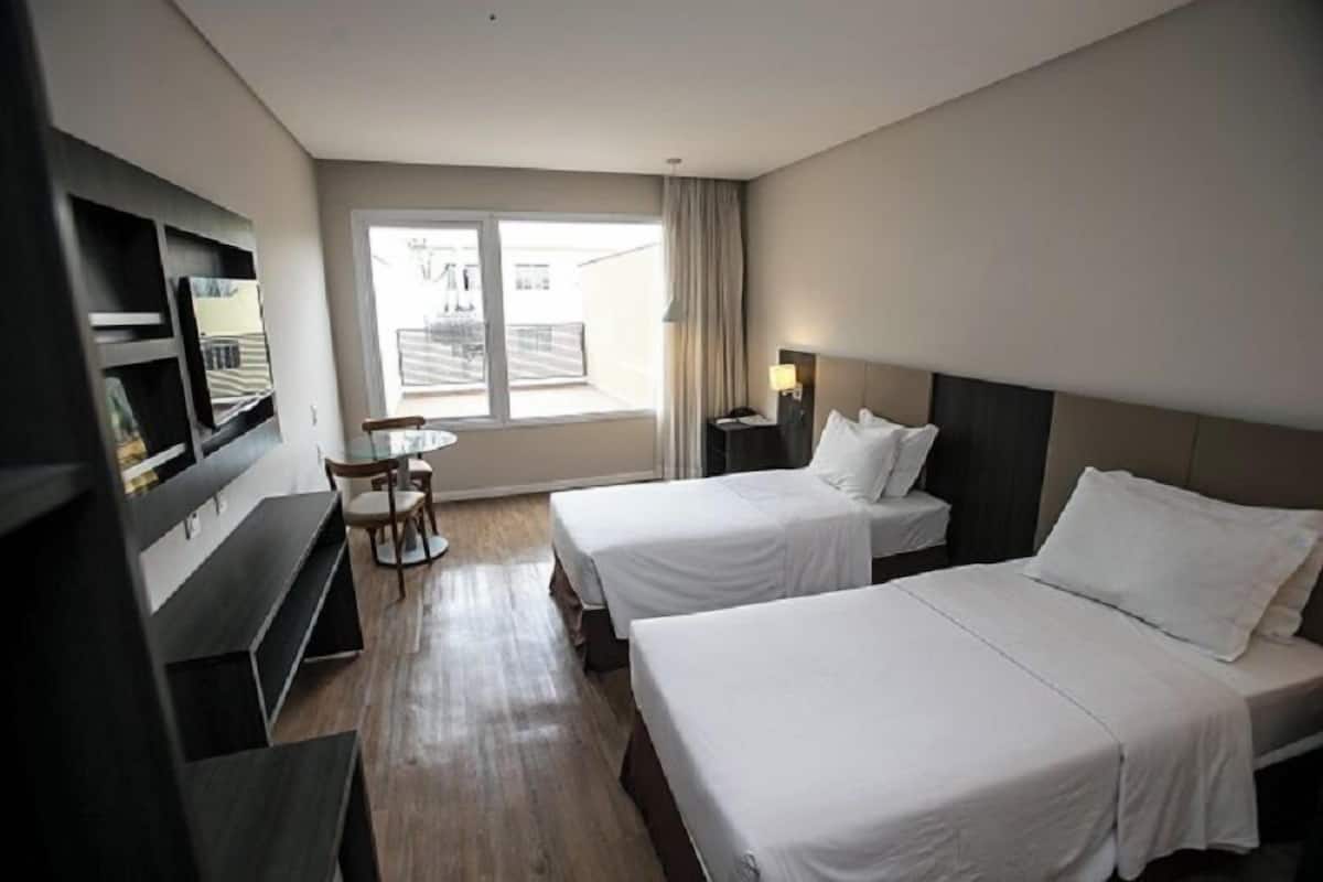 Ein Hotelzimmer mit zwei Betten, einem Fernseher, einem Schreibtisch und einem Fenster mit Vorhängen.