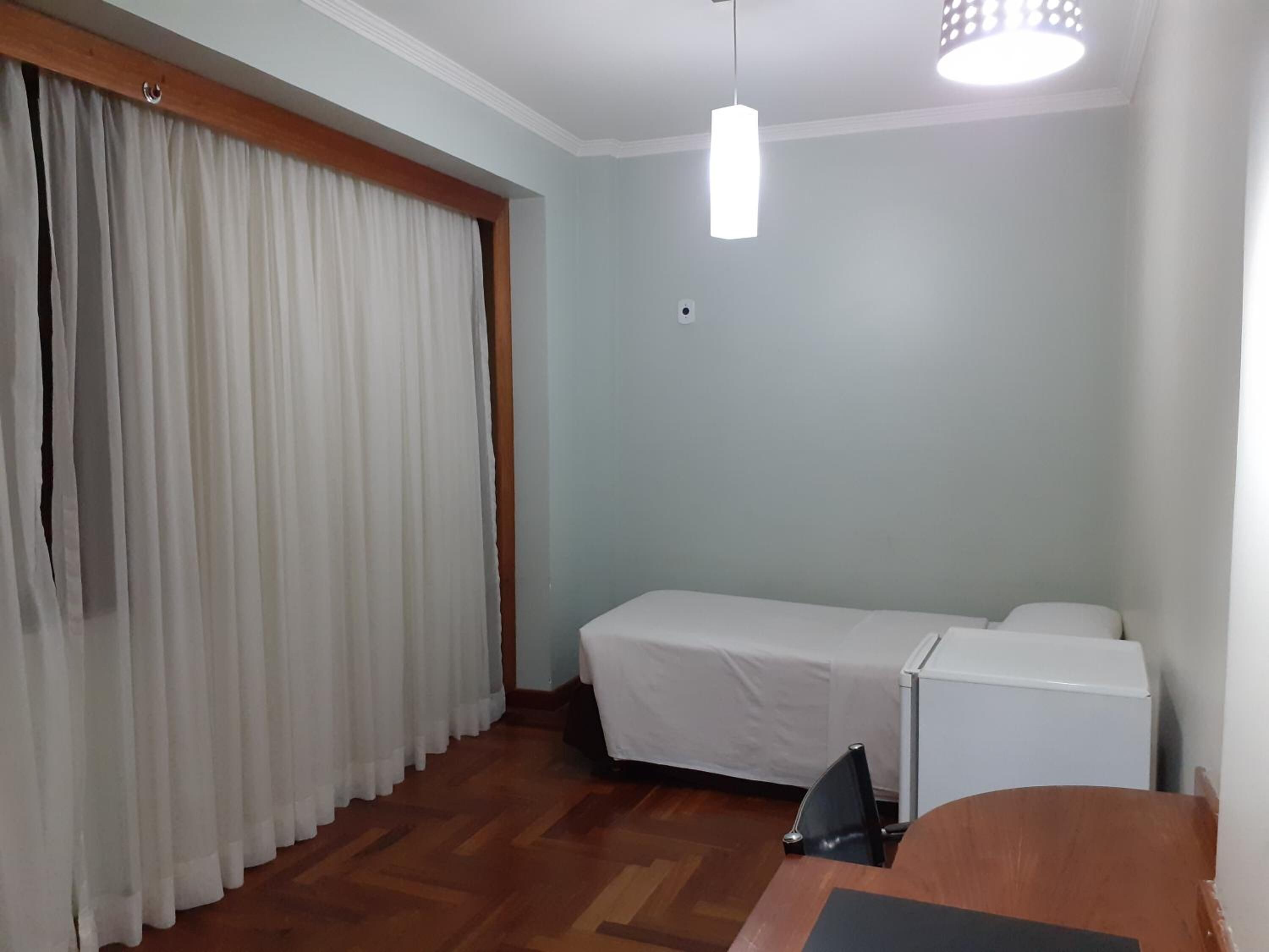 A hotel room with a bed, a desk, a chair, a wardrobe, and a ceiling light.