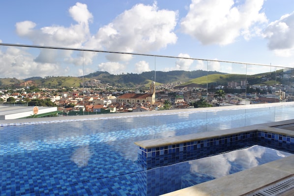 A pool with a tiled edge and a view of a town with buildings and hills in the background.
