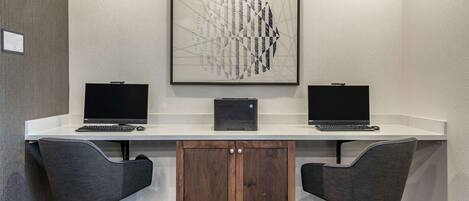 A conference room with two desks, each with a computer and chair, and a wooden cabinet below.