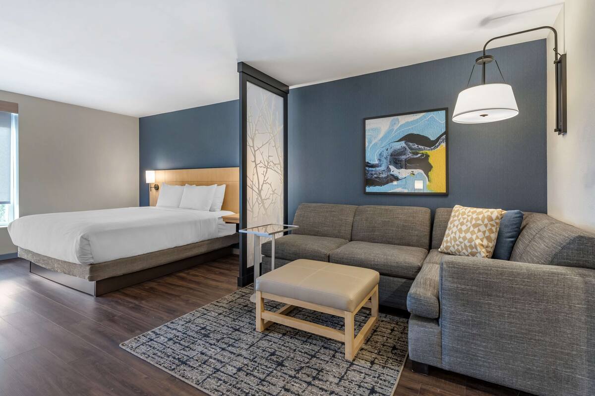 A modern hotel room with a bed, sofa, and a small table.