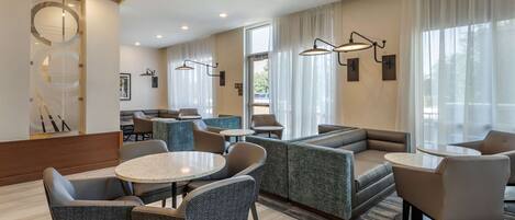 Eine moderne Hotelhalle mit Sitzbereichen, einem Empfangsbereich und großen Fenstern.