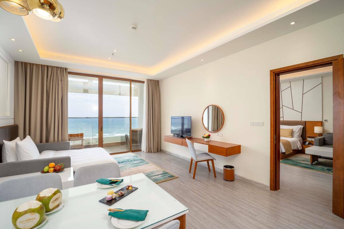 Habitación de hotel con balcón, escritorio, cama y zona de estar.