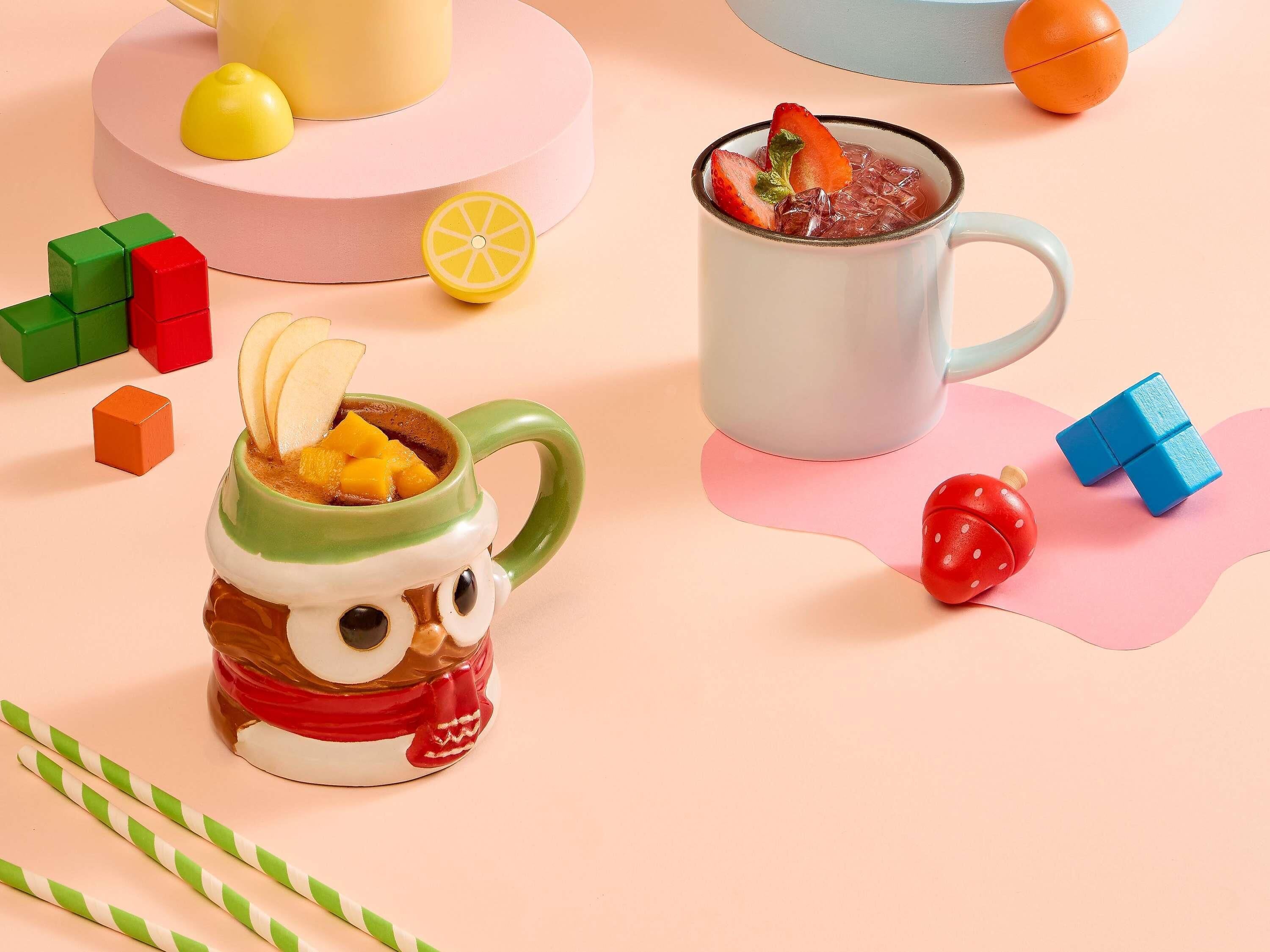 A mug with a face, a cup with fruit, and colorful blocks.