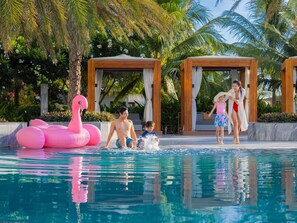 A swimming pool with inflatable flamingos, palm trees, and wooden structures in the background. - Mövenpick Resort Cam Ranh (Cam Lam)