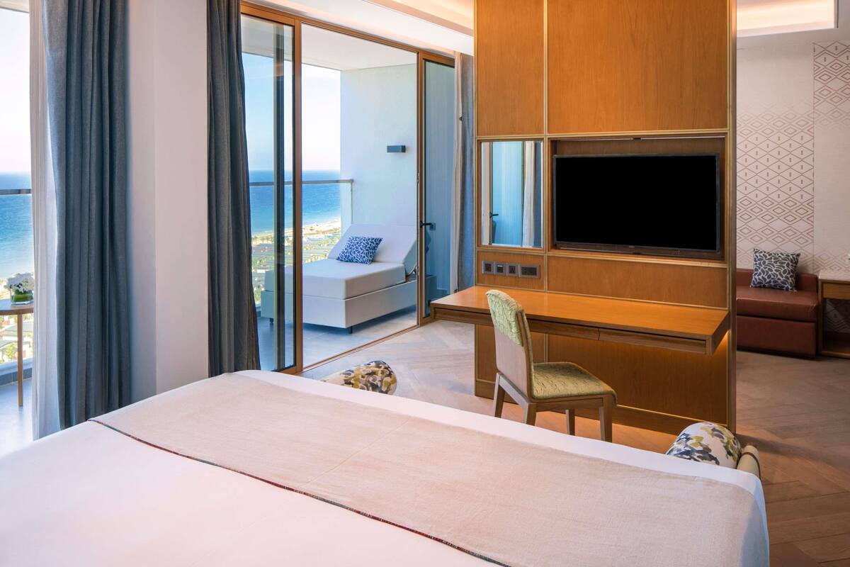 Habitación de hotel con cama, escritorio, televisor, silla y vista al océano.