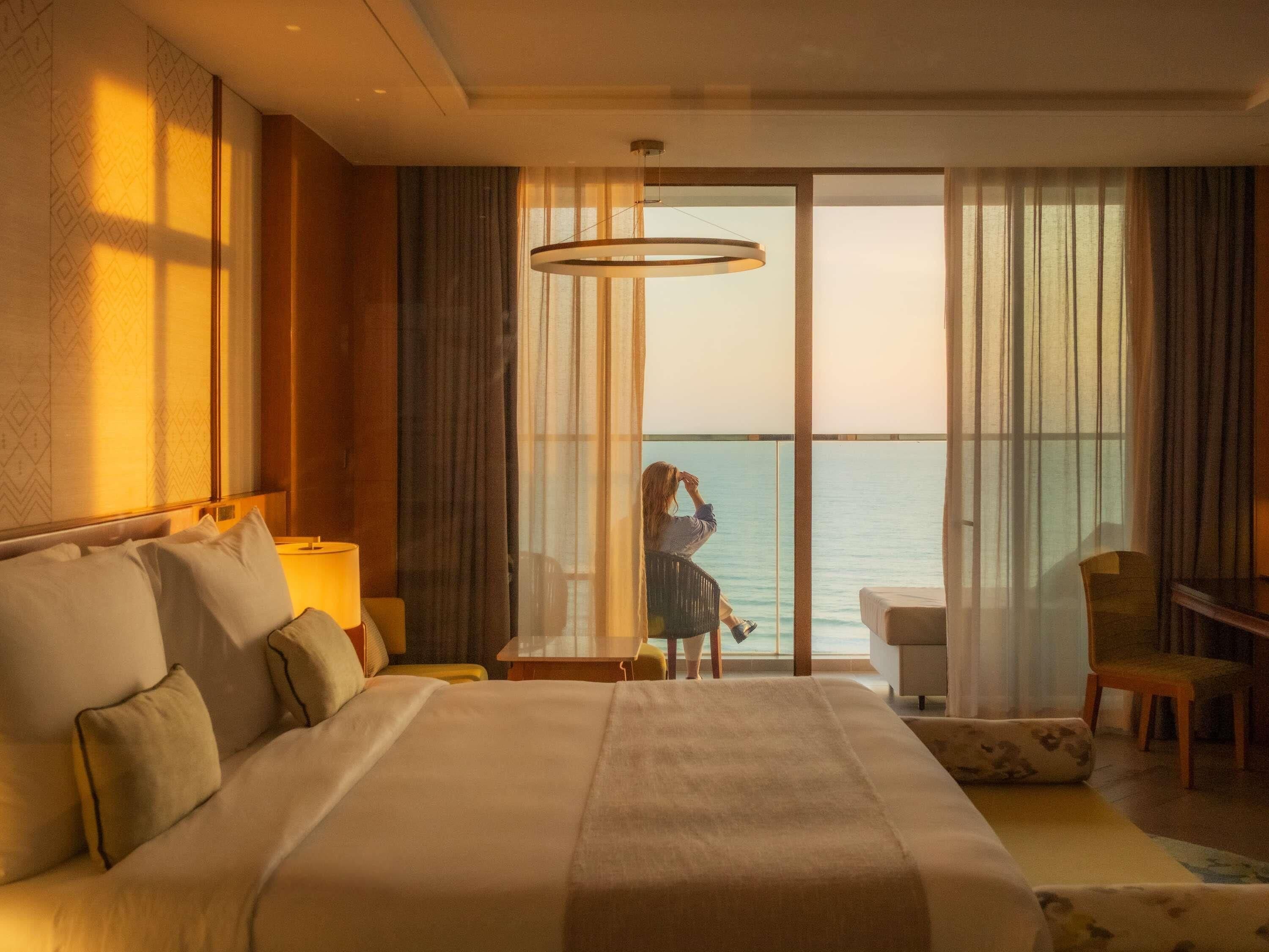 A hotel room with a large bed, a desk, a chair, and a view of the sea.