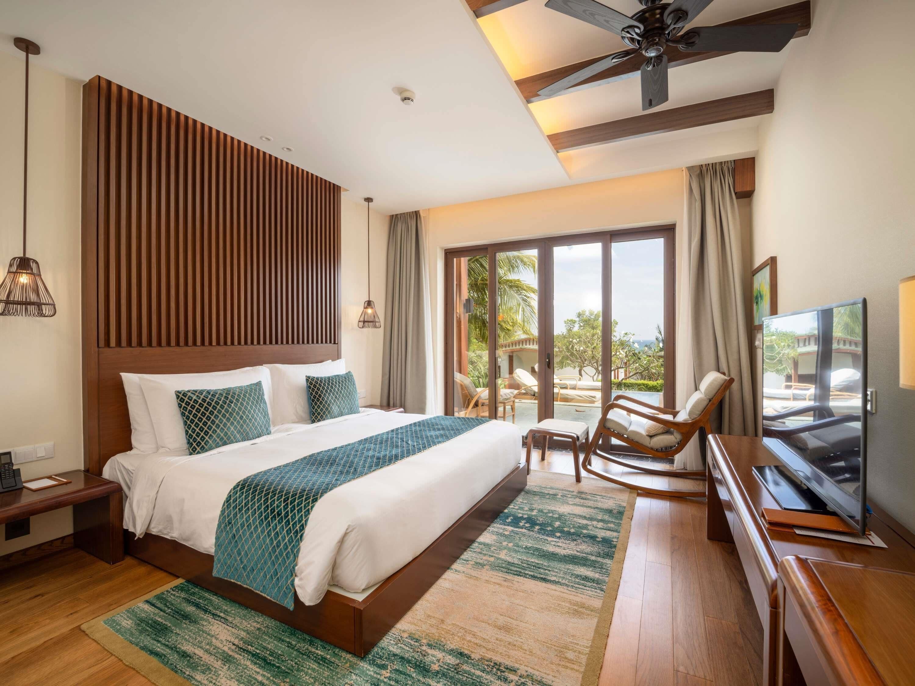 A hotel room with a large bed, a TV, a ceiling fan, and a view of the outdoors.
