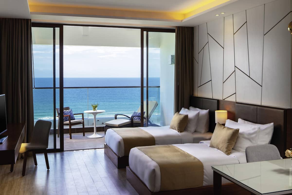 Habitación de hotel con dos camas, una mesa de vidrio, una silla y vista al océano.