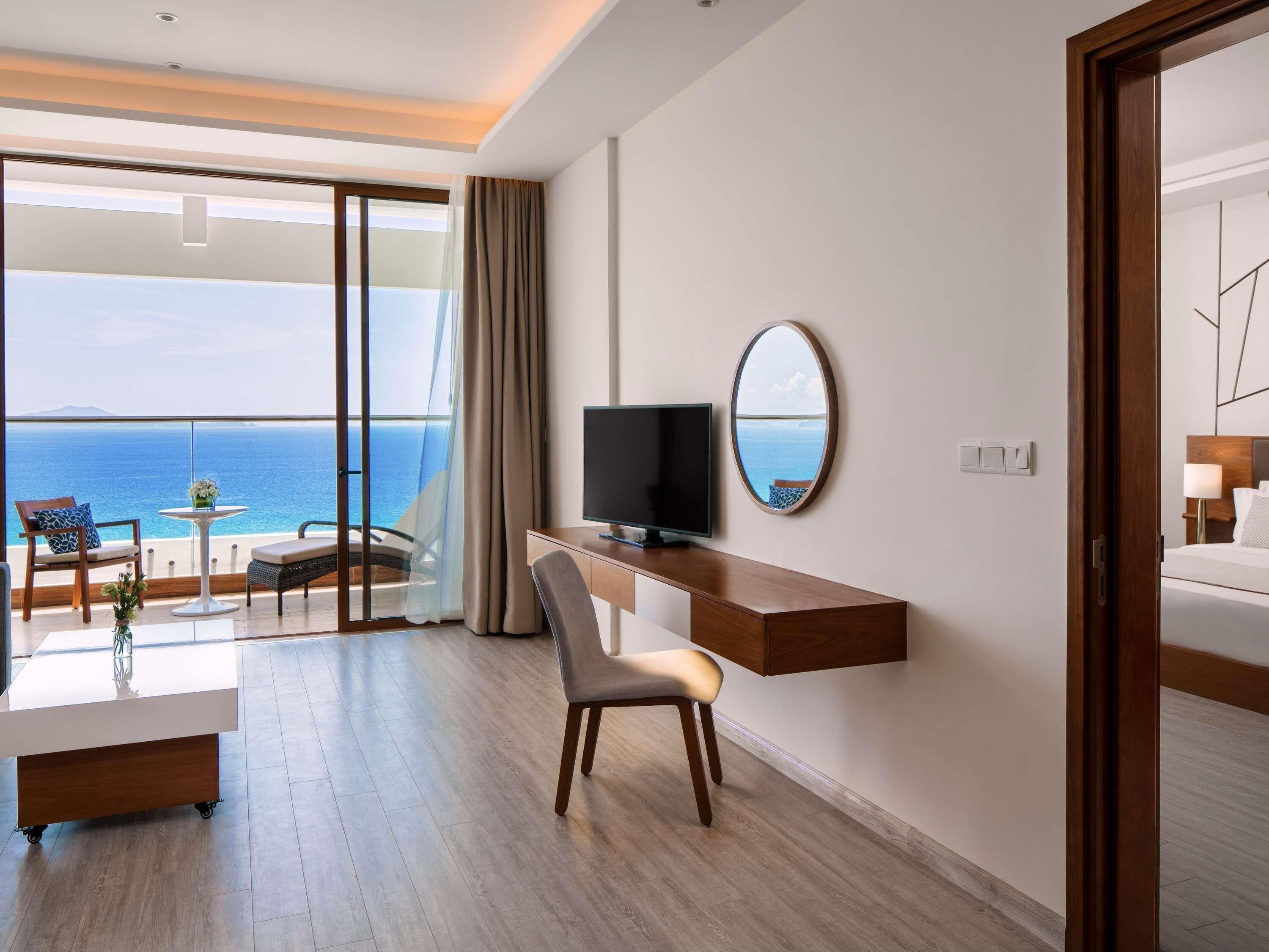 A hotel room with a balcony, a desk, a chair, a television, and a bed.