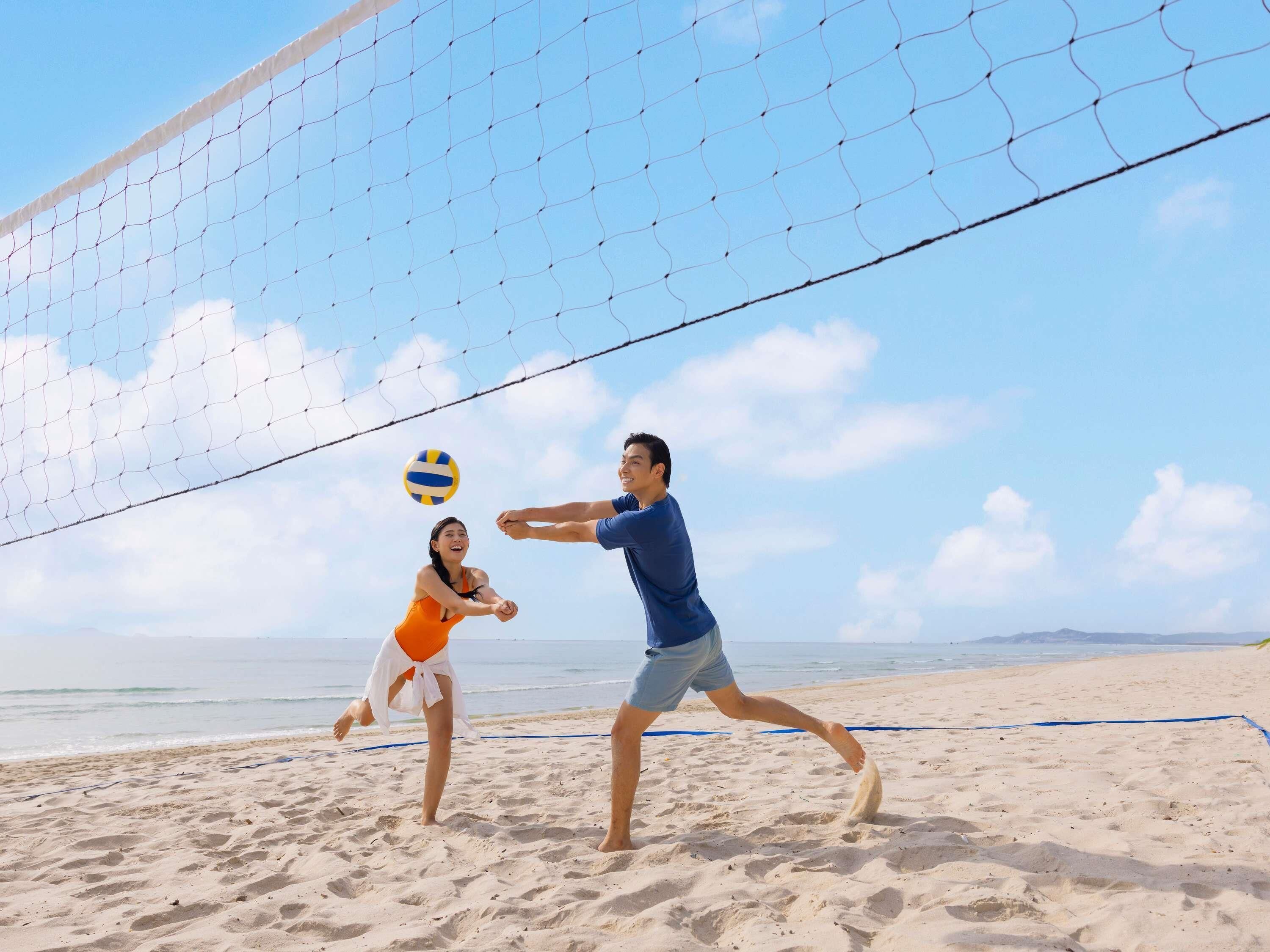 A beach volleyball game with a clear sky and ocean in the background.