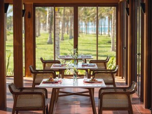 Un espace extérieur aménagé pour les repas, avec des tables et des chaises, une vue sur un paysage verdoyant et des palmiers, ainsi qu’une structure en forme de pergola en bois.