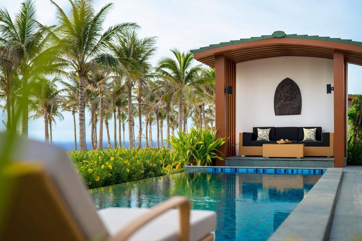 Zona de piscina con una silla de salón, un sofá con cojines y una pared decorativa.