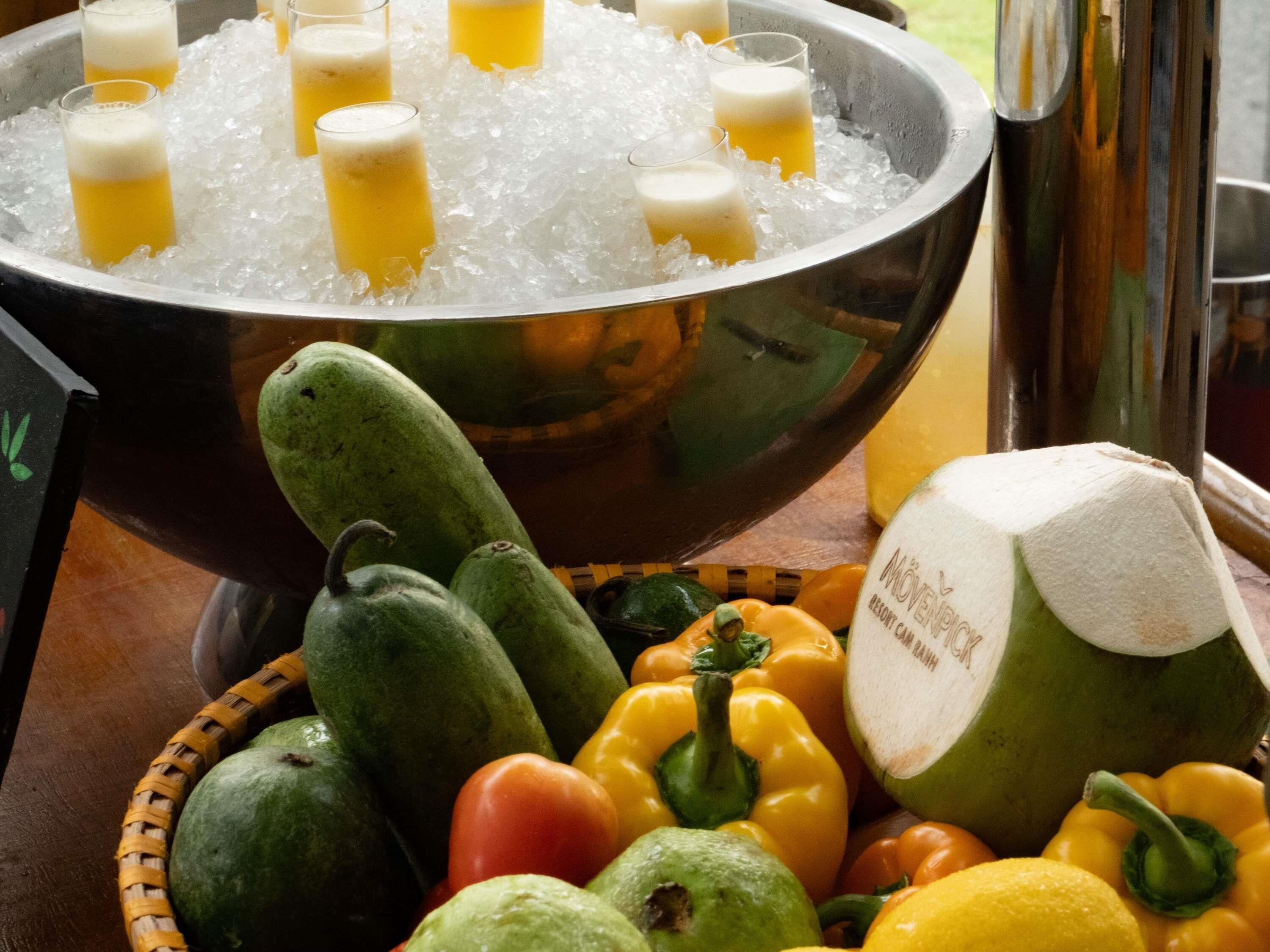 A bowl of ice with drinks, a basket of vegetables, and a coconut.