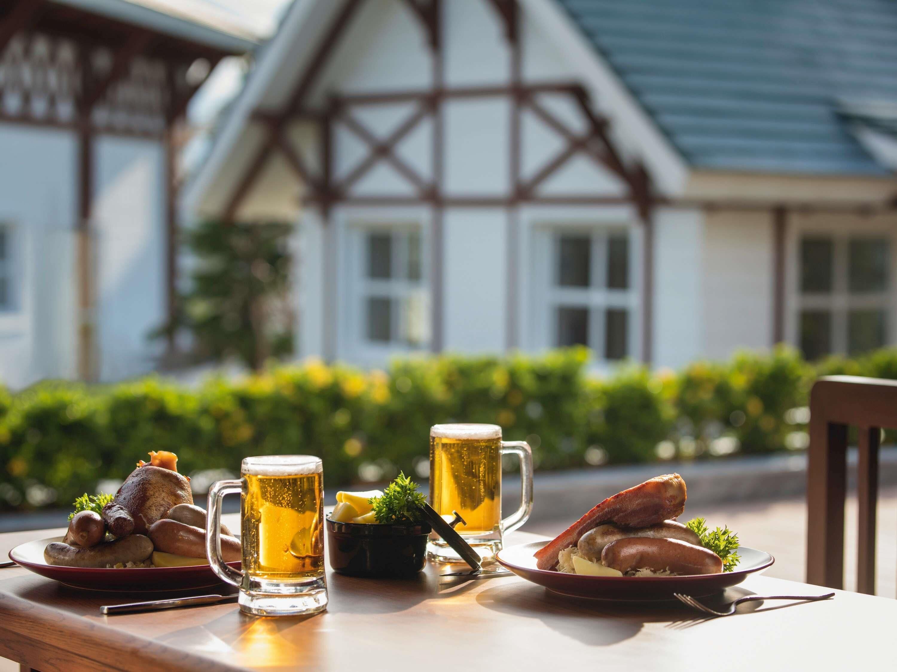 A dining table with beer mugs and plates of food, set outdoors with a building in the background.