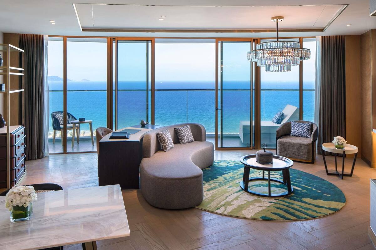 Una sala moderna con un ventanal grande con vistas al mar, una araña y una mesa de centro redonda.