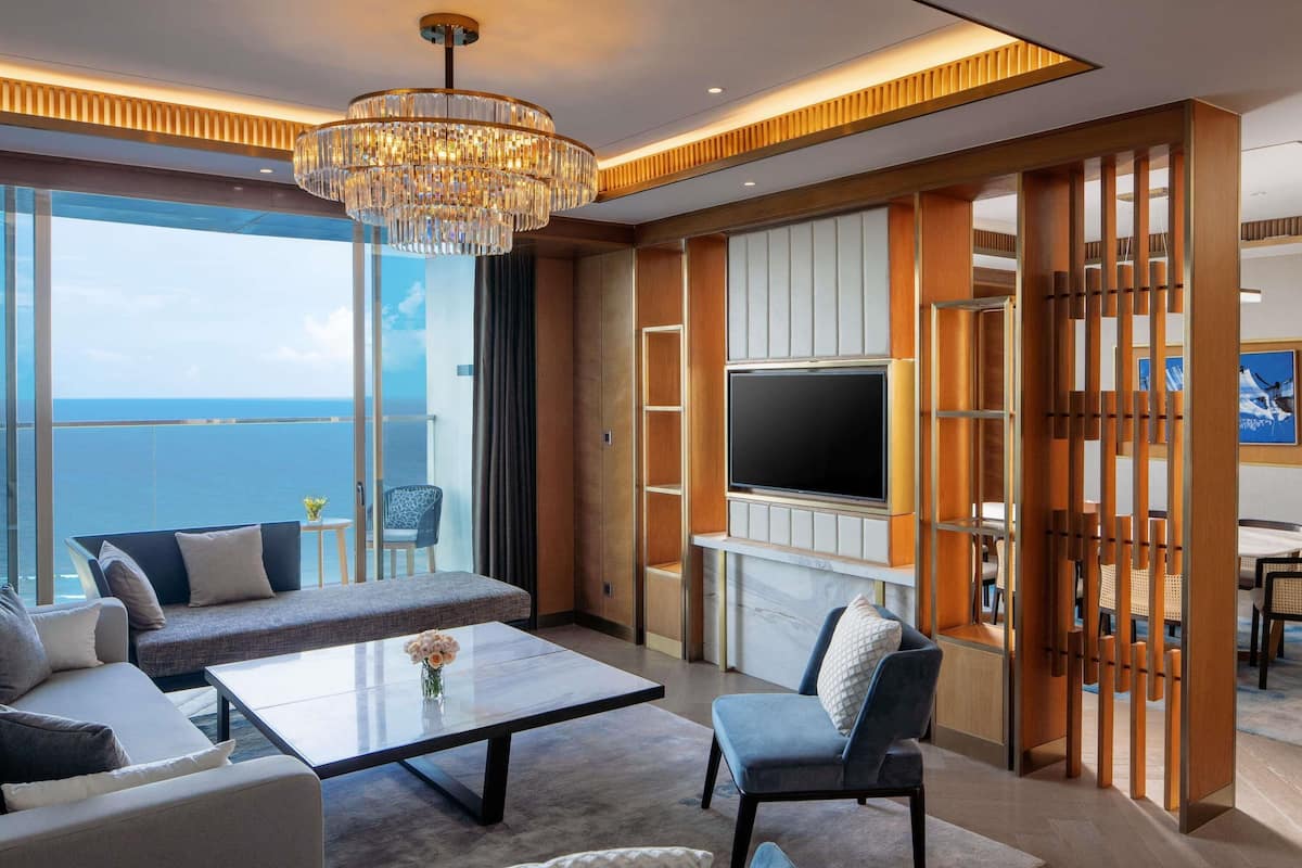 A modern living room with a large TV, seating area, and a view of the ocean.
