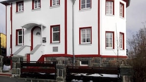 A two-story building with a white facade and red trim, featuring a stone base and a small porch with steps. - Ferienhaus XXL Deutschland (Schwarzatal)